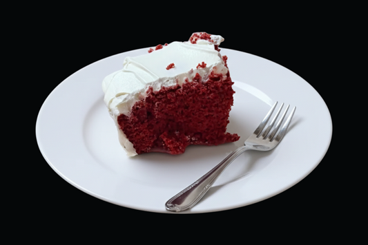 Slice of red velvet cake with white frosting on a white plate with a fork against a black background